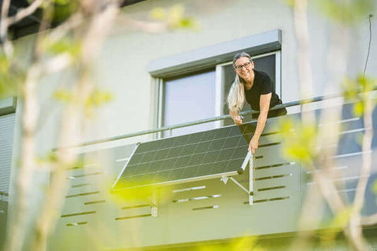 Woman installing a solar panel on a balcony, showcasing steckerfertige Photovoltaikanlagen.